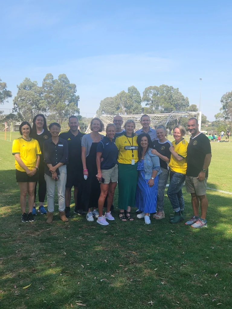 Committee members and families lined up in front of the goals at Anderson Park on a clear day.