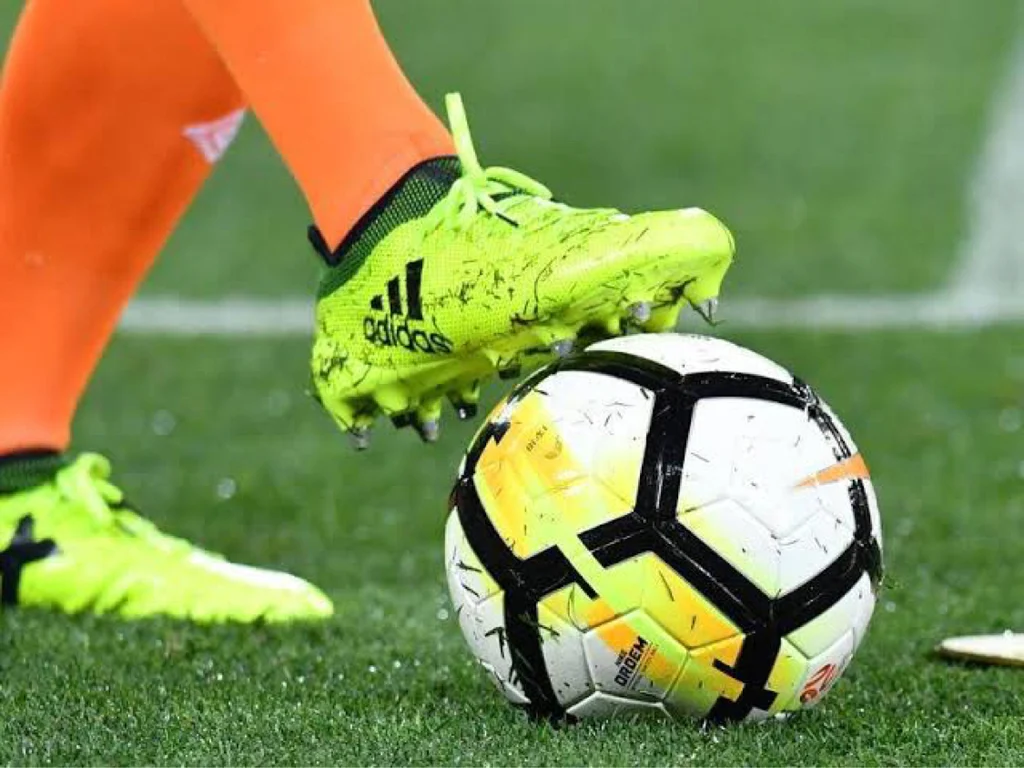 Close-up of a player’s boot resting on a match ball on the pitch.